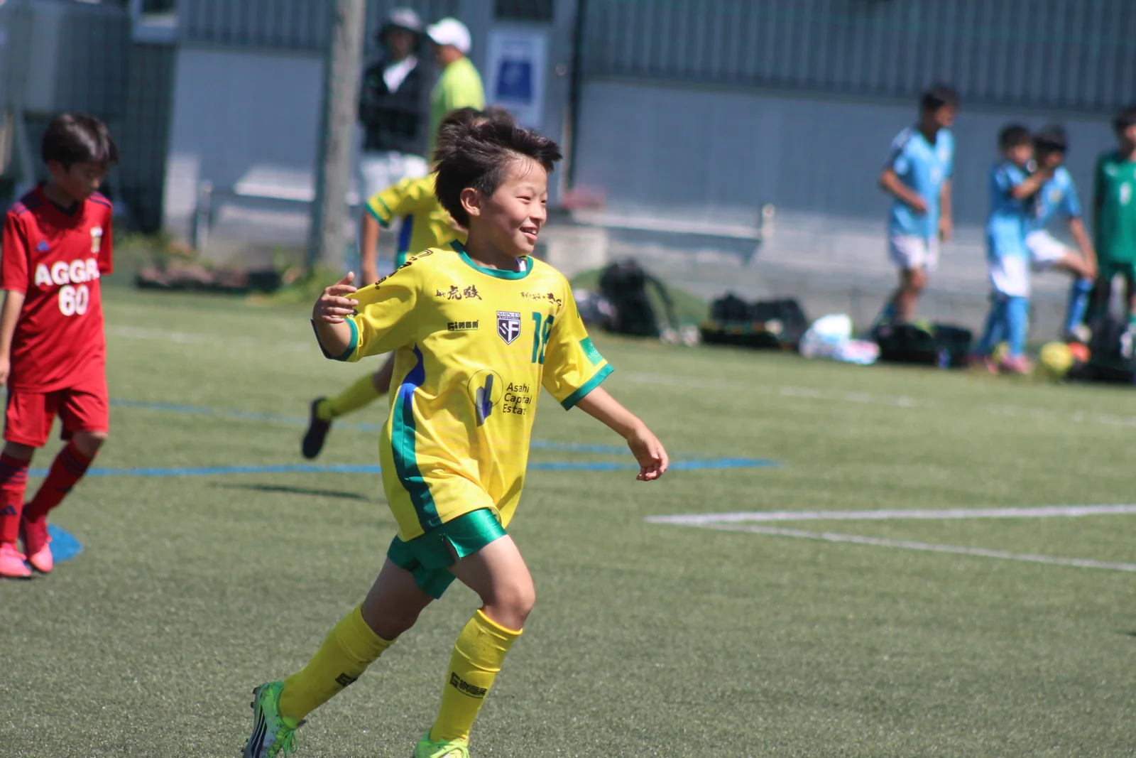 ピッチを走る黄色いユニフォームの真栄FCの選手